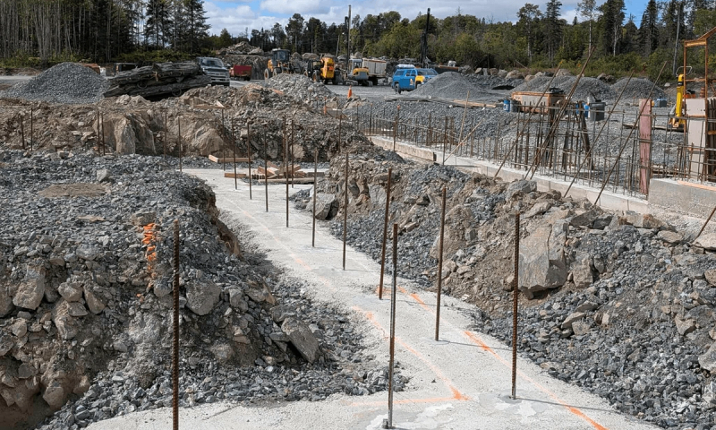 Piles of stone and foundations with rebar sticking out of them at the construction site of the Anishnawbe G’Zhiitoonegamic modular home factory near Kirkland Lake, Ontario.