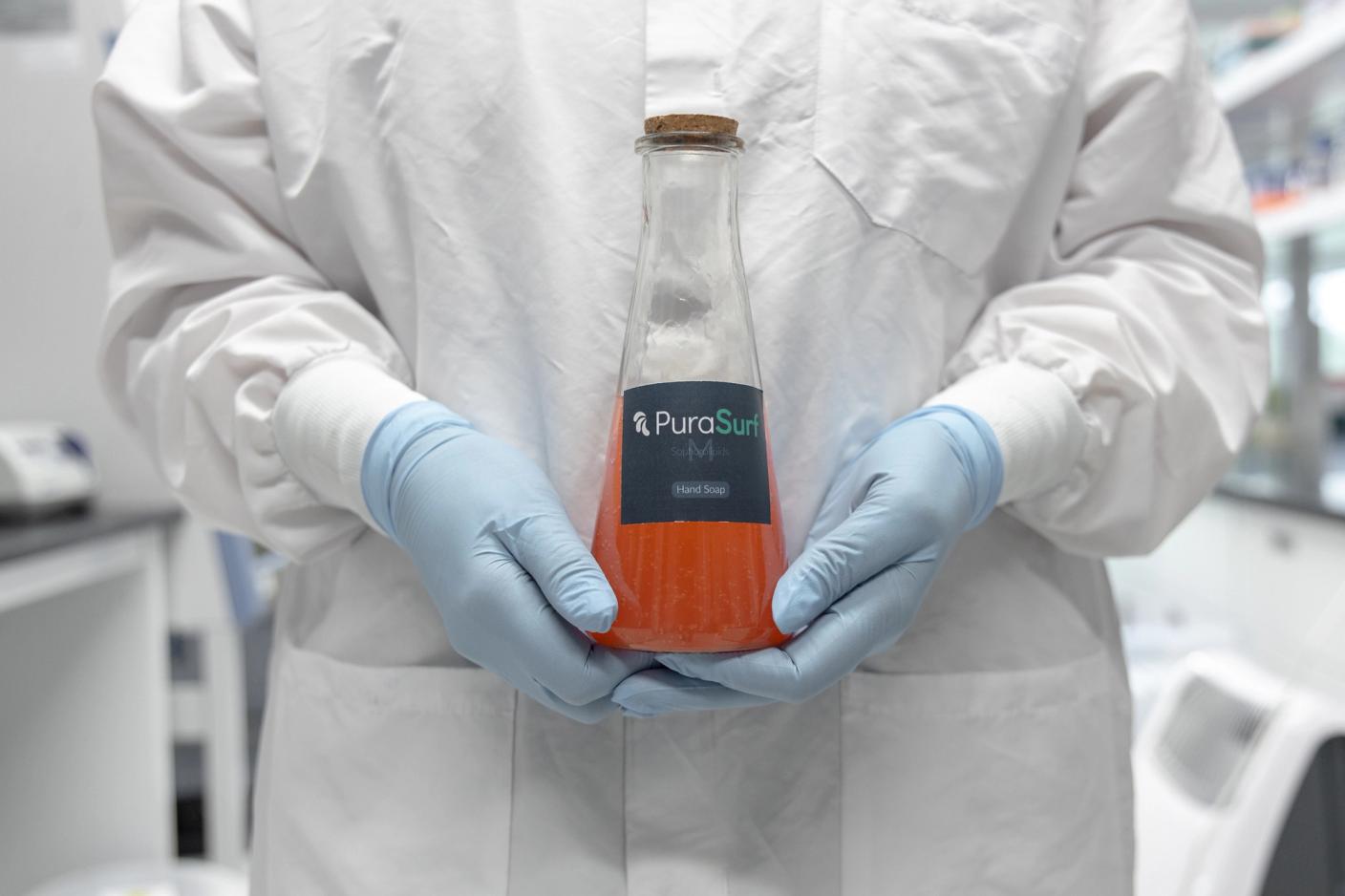 In the laboratory of Dispersa, a scientist holds a beaker of PuraSurf, its first cleaning ingredient.
