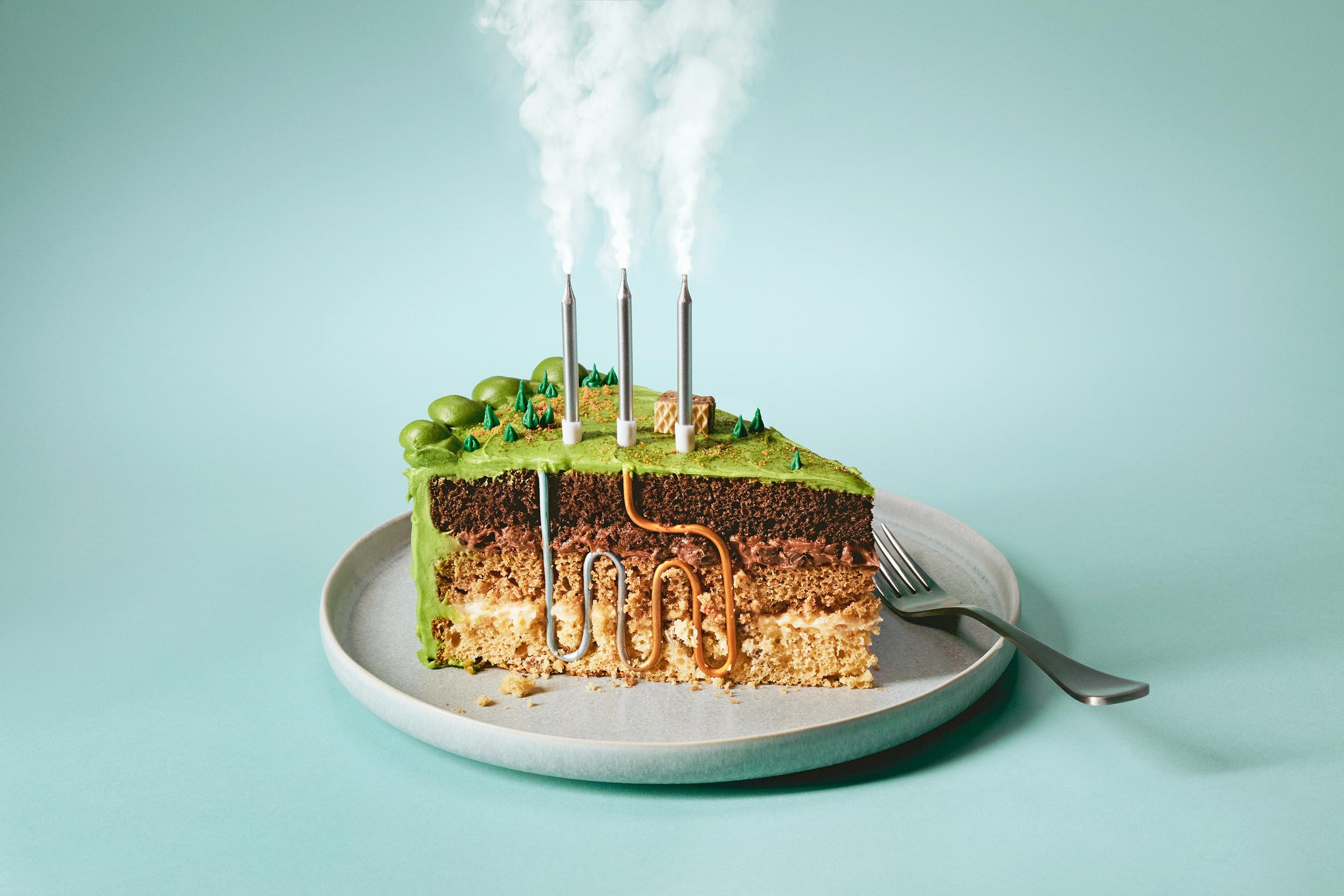 A slice of cake with green icing designed to look like layers of the Earth’s crust, with silver candles representing steam and a series of pipes winding through the layers of the cake to illustrate a piece on next-gen geothermal energy in Canada.