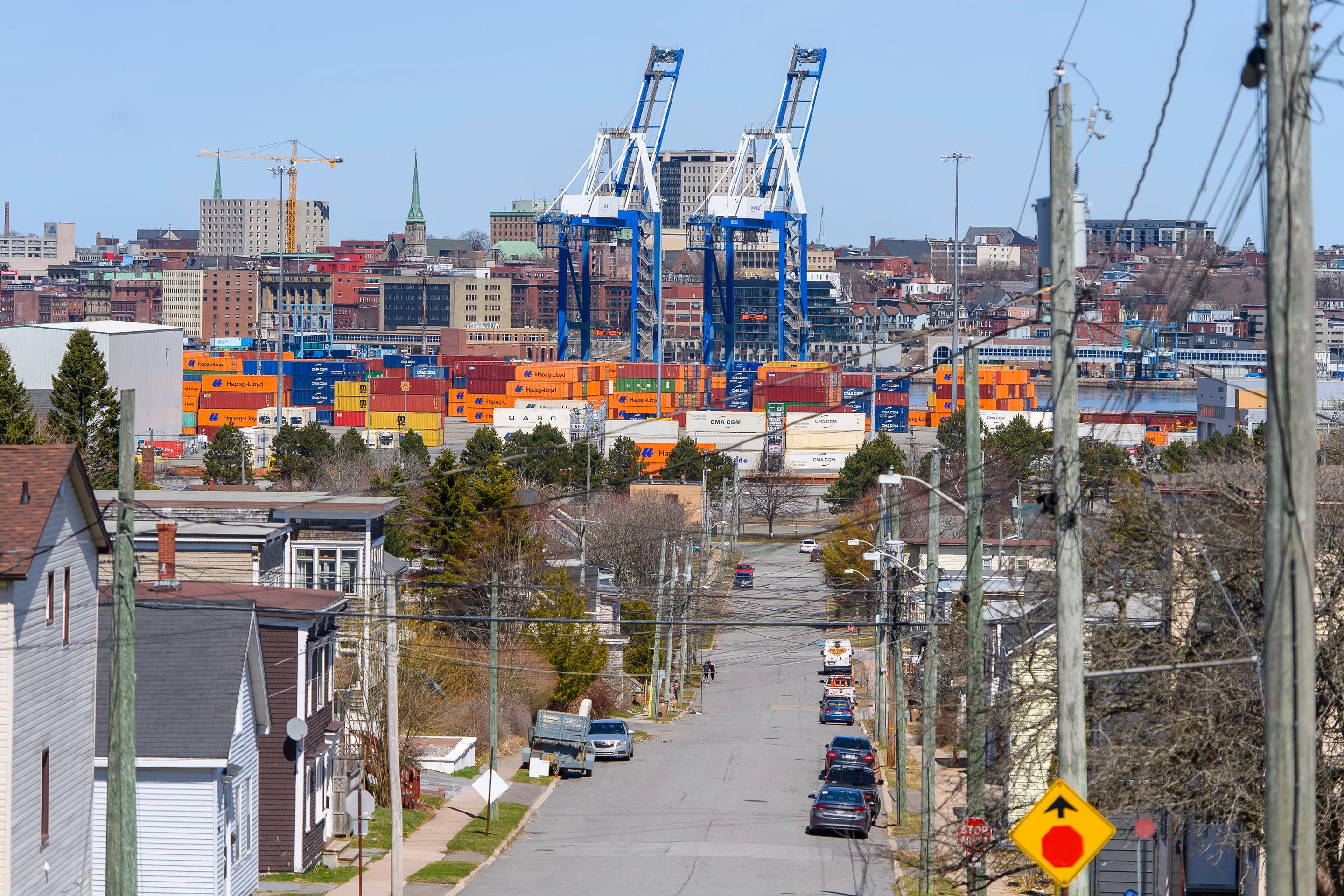 A photo illustration of a cargo ship with the Hapag-LLoyd name on the site and a crane behind it with people walking in the foreground across the water at the Port of Saint John