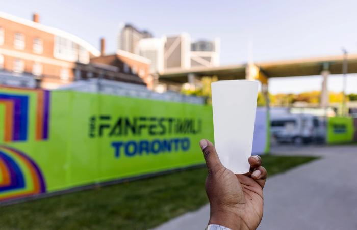 handing holding a reusable plastic cup in front of a green sign that says 'Fan Festival Toronto'