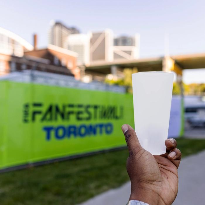 handing holding a reusable plastic cup in front of a green sign that says 'Fan Festival Toronto'