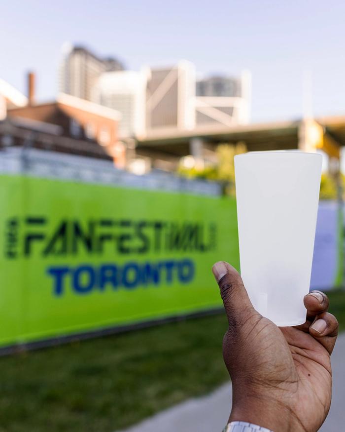 handing holding a reusable plastic cup in front of a green sign that says 'Fan Festival Toronto'