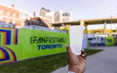 handing holding a reusable plastic cup in front of a green sign that says 'Fan Festival Toronto'