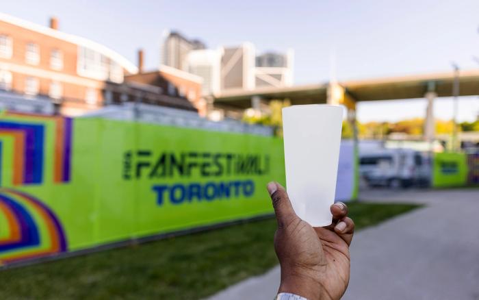 handing holding a reusable plastic cup in front of a green sign that says 'Fan Festival Toronto' 
