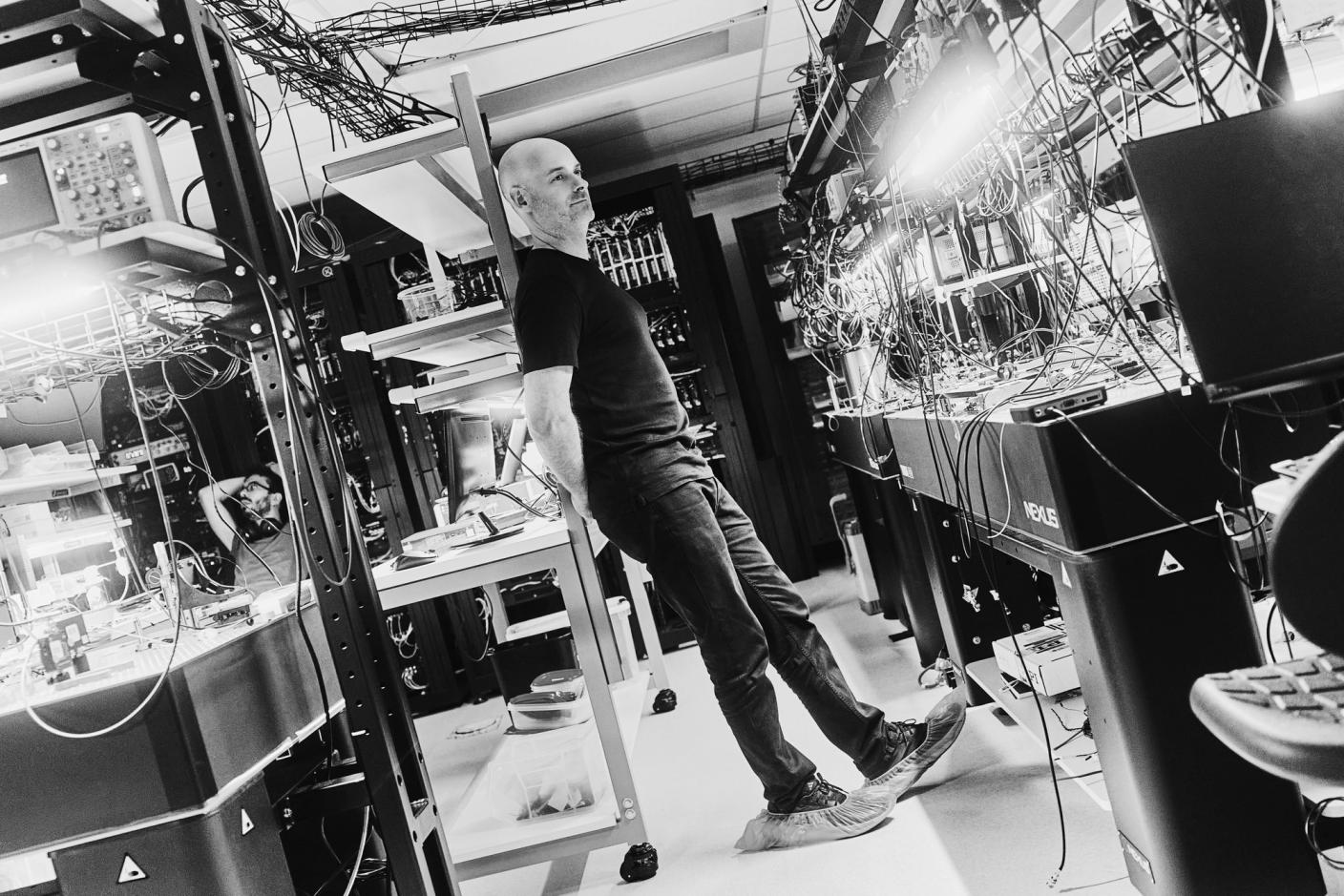 Black and white photo of Christian Weedbrook in front of computers