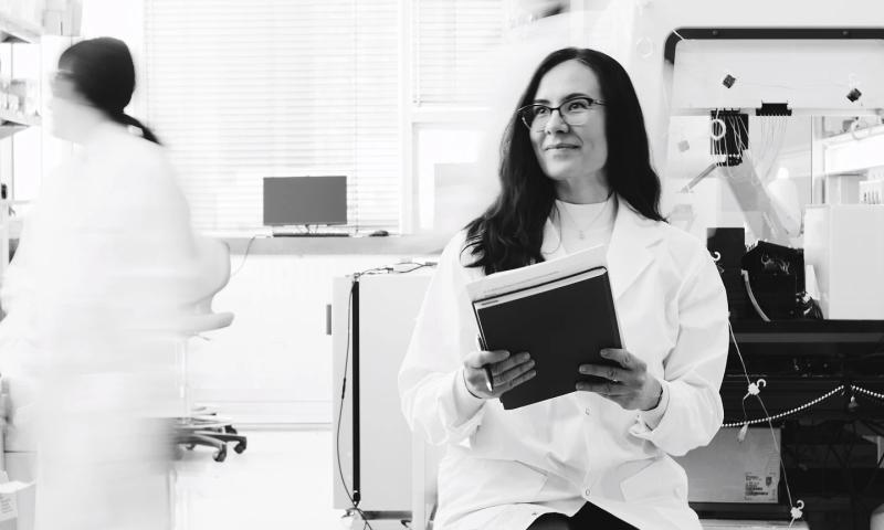 A portrait of the University of Toronto professor Milica Radisic, wearing a white lab coat and holding a folder and a pen. 