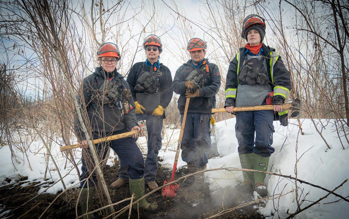 A group shot of the team hunting zombie fires in Canada, showing four people in wildfire fighting gear, From left to right: Sonja Leverkus, Ecosystem Scientist, Senior Fire Lead, Northern Fire WoRx (NFWRx); Donovan Bertrand, Crew Leader NFWRx, member of Acho Dene Koe; David Wilmsmeier, Crew Leader NFWRx, member of Prophet River First Nation; Alexis Jorgensen, Ecologist, NFWRx, Fort Nelson, B.C.