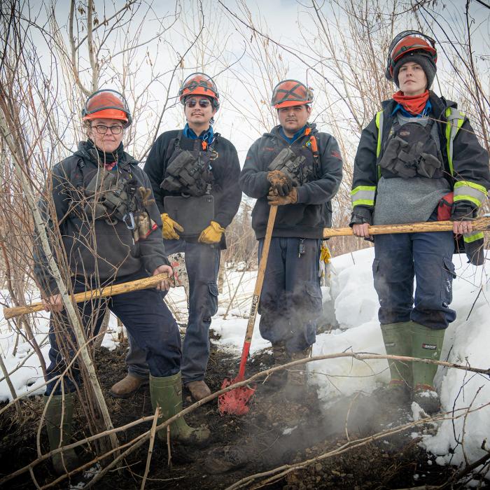 A group shot of the team hunting zombie fires in Canada, showing four people in wildfire fighting gear, From left to right: Sonja Leverkus, Ecosystem Scientist, Senior Fire Lead, Northern Fire WoRx (NFWRx); Donovan Bertrand, Crew Leader NFWRx, member of Acho Dene Koe; David Wilmsmeier, Crew Leader NFWRx, member of Prophet River First Nation; Alexis Jorgensen, Ecologist, NFWRx, Fort Nelson, B.C.