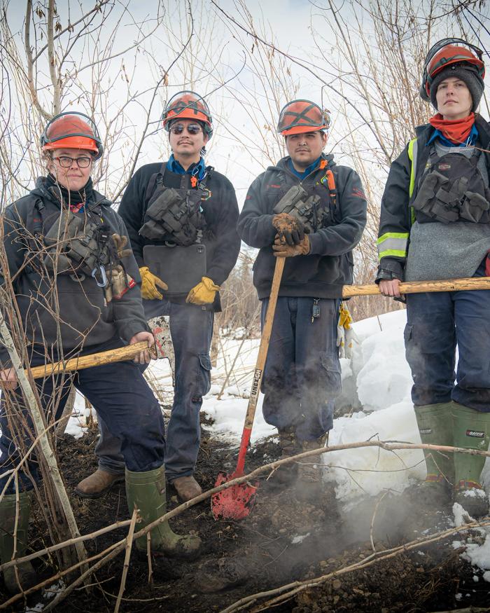A group shot of the team hunting zombie fires in Canada, showing four people in wildfire fighting gear, From left to right: Sonja Leverkus, Ecosystem Scientist, Senior Fire Lead, Northern Fire WoRx (NFWRx); Donovan Bertrand, Crew Leader NFWRx, member of Acho Dene Koe; David Wilmsmeier, Crew Leader NFWRx, member of Prophet River First Nation; Alexis Jorgensen, Ecologist, NFWRx, Fort Nelson, B.C.