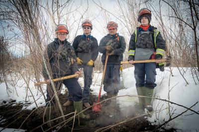 A group shot of the team hunting zombie fires in Canada, showing four people in wildfire fighting gear, From left to right: Sonja Leverkus, Ecosystem Scientist, Senior Fire Lead, Northern Fire WoRx (NFWRx); Donovan Bertrand, Crew Leader NFWRx, member of Acho Dene Koe; David Wilmsmeier, Crew Leader NFWRx, member of Prophet River First Nation; Alexis Jorgensen, Ecologist, NFWRx, Fort Nelson, B.C.