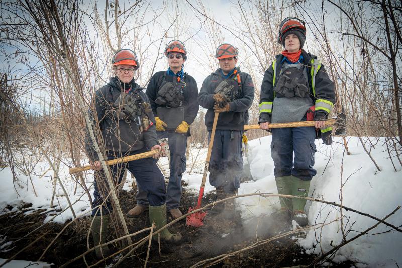 A group shot of the team hunting zombie fires in Canada, showing four people in wildfire fighting gear, From left to right: Sonja Leverkus, Ecosystem Scientist, Senior Fire Lead, Northern Fire WoRx (NFWRx);  Donovan Bertrand, Crew Leader NFWRx, member of Acho Dene Koe; David Wilmsmeier, Crew  Leader NFWRx, member of Prophet River First Nation; Alexis Jorgensen, Ecologist, NFWRx,  Fort Nelson, B.C.