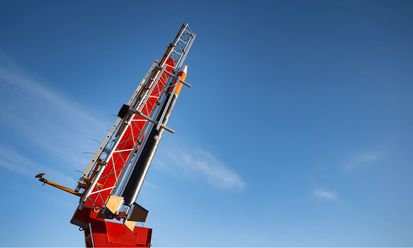 A red rocket launch pad viewed from below against a deep blue sky