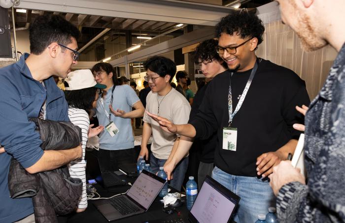 Students wearing badges on lanyards – TinyTPU's Evan Lin, Kenny Guo, Xander Chin and Surya Sure – demonstrating their innovations on laptops and smiling at the 2026 Socratica Symposium, a weekend-long University of Waterloo event in Kitchener, Ont.