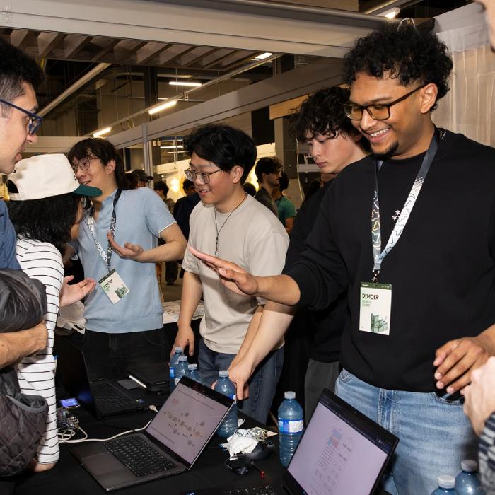 Students wearing badges on lanyards – TinyTPU's Evan Lin, Kenny Guo, Xander Chin and Surya Sure – demonstrating their innovations on laptops and smiling at the 2026 Socratica Symposium, a weekend-long University of Waterloo event in Kitchener, Ont.