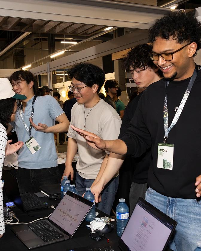 Students wearing badges on lanyards – TinyTPU's Evan Lin, Kenny Guo, Xander Chin and Surya Sure – demonstrating their innovations on laptops and smiling at the 2026 Socratica Symposium, a weekend-long University of Waterloo event in Kitchener, Ont.