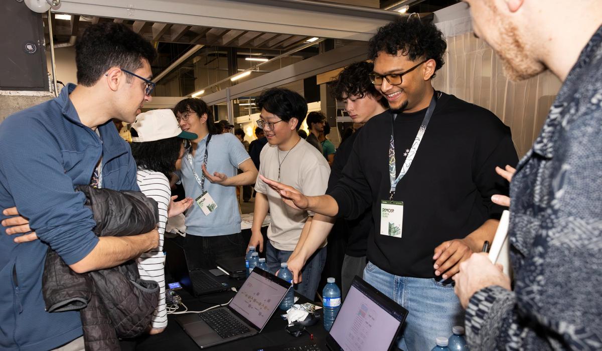 Students wearing badges on lanyards – TinyTPU's Evan Lin, Kenny Guo, Xander Chin and Surya Sure – demonstrating their innovations on laptops and smiling at the 2026 Socratica Symposium, a weekend-long University of Waterloo event in Kitchener, Ont. 
