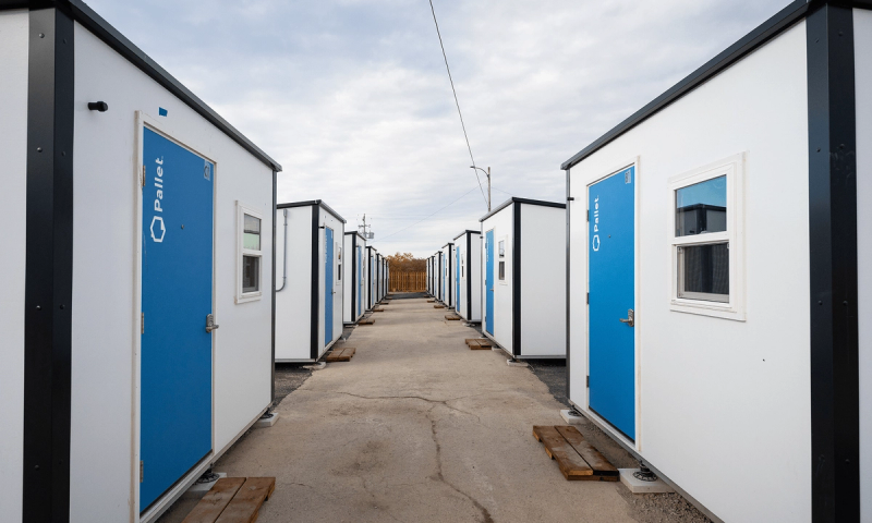A view down a passage between the small prefabricated shelters at the Village at Pine Tree Park on the outskirts of Sydney, N.S., showing the blue front doors and white building fronts with small windows