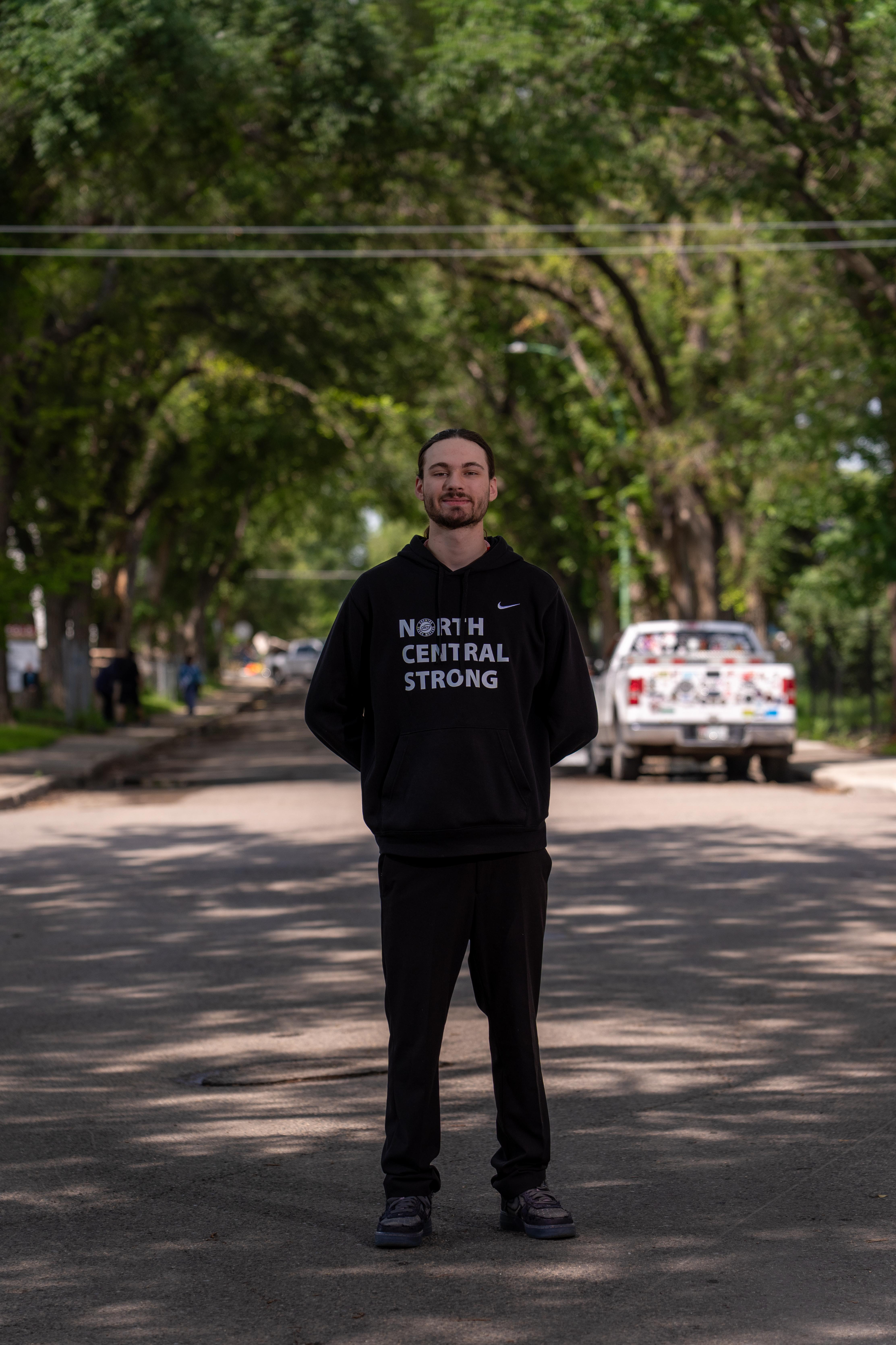 CG Hockley-Lonechild stands in a street wearing a North Central Strong hoodie.
