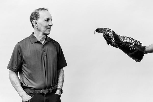 A portrait of the endocrinologist Dr. Daniel Drucker, next to a Gila monster being held by a hand wearing a glove for a longread profile of him and his path to GLP-1s and Ozempic