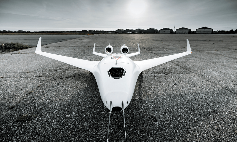 An aerial view of the Bombardier EcoJet flying over a rocky shoreline with grassy fields and trees in the background