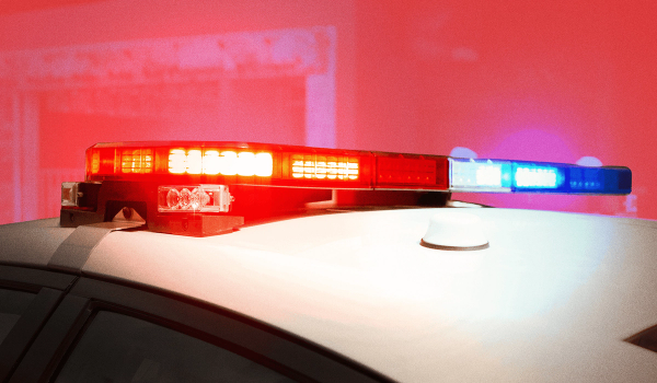 A photo illustration of a flashing police vehicle siren, shown in closeup on top of a white vehicle, against a reddish illustration background, for a piece on AI use for 911 calls in Canada