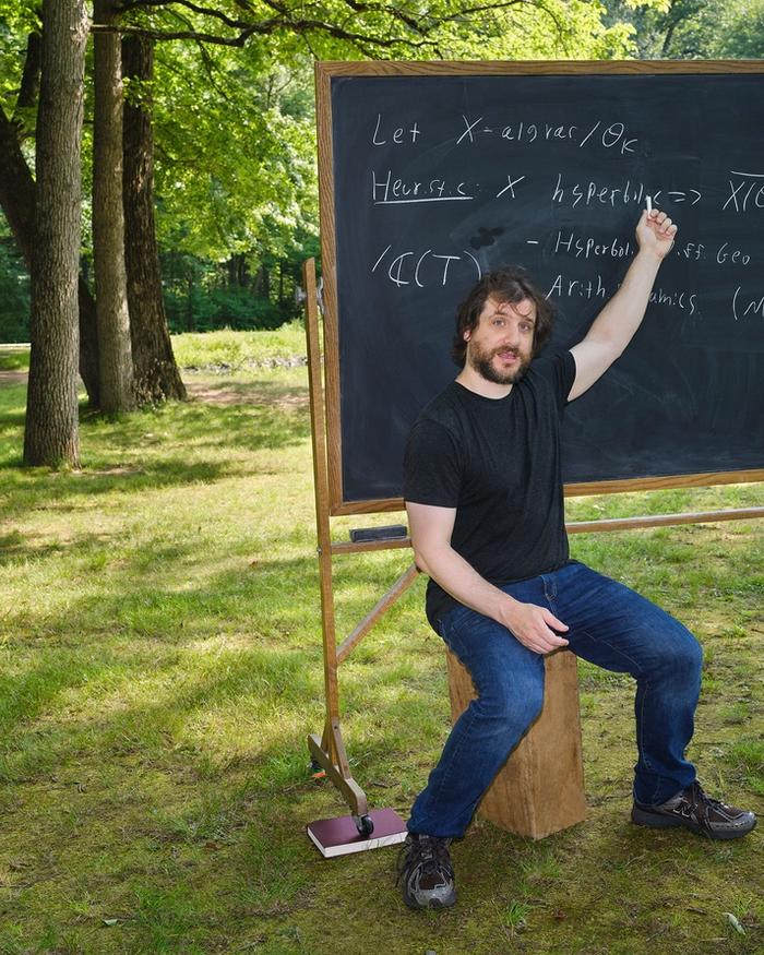 Jacob Tsimerman sits in a field, writing equations on a chalkboard.