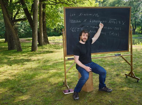 Jacob Tsimerman sits in a field, writing equations on a chalkboard.