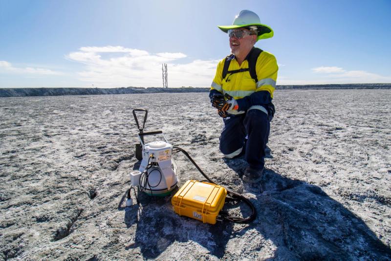 Dr. Greg Dipple, co-founder and head of science at Arca Climate, kneels at a mine site next to some equipment.