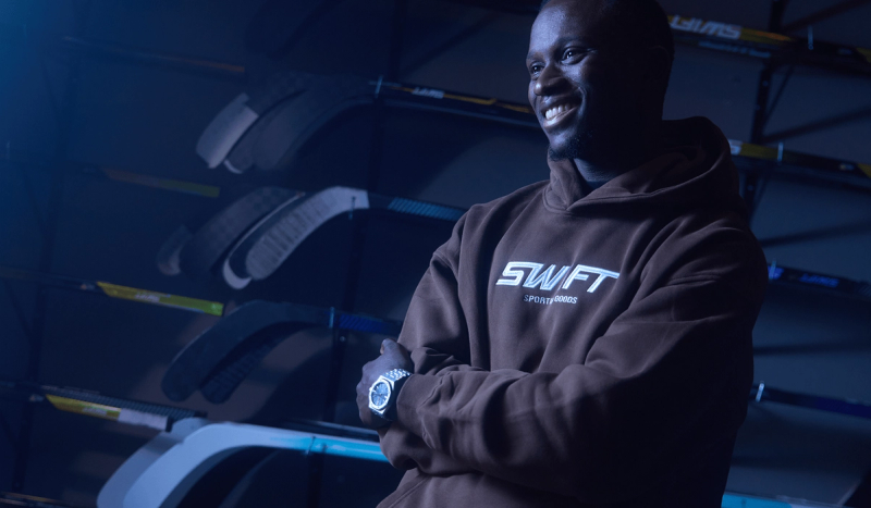 Zechary Thomas posing in front of a wall of hockey sticks