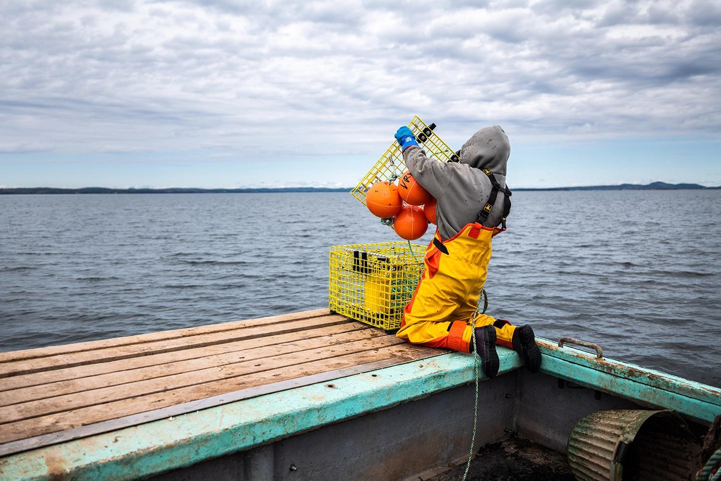 A fisher working on a crate for a ropeless fishing system and holding a crate filled with orange balloons