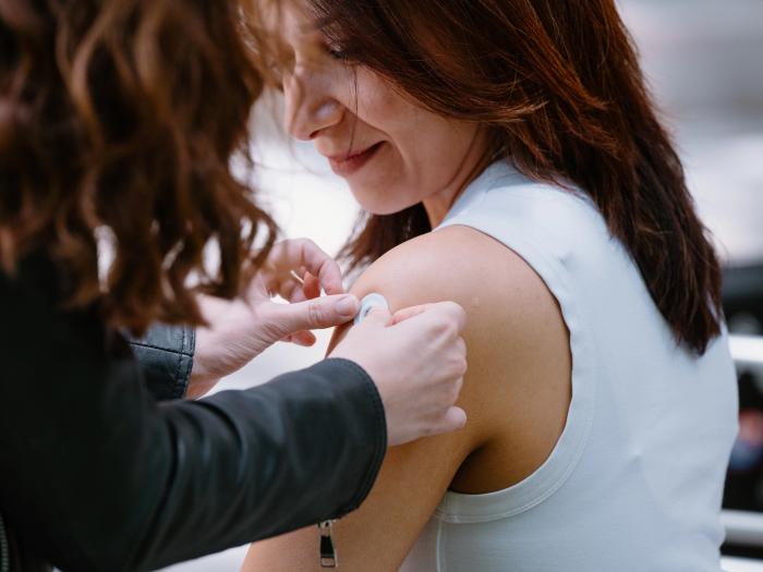 A portrait of Mahla Poudineh wearing gloves and holding tweezers that hold her co-creation, the the Wearable Aptalyzer, a painless wearable device that can track molecules in the body in real time