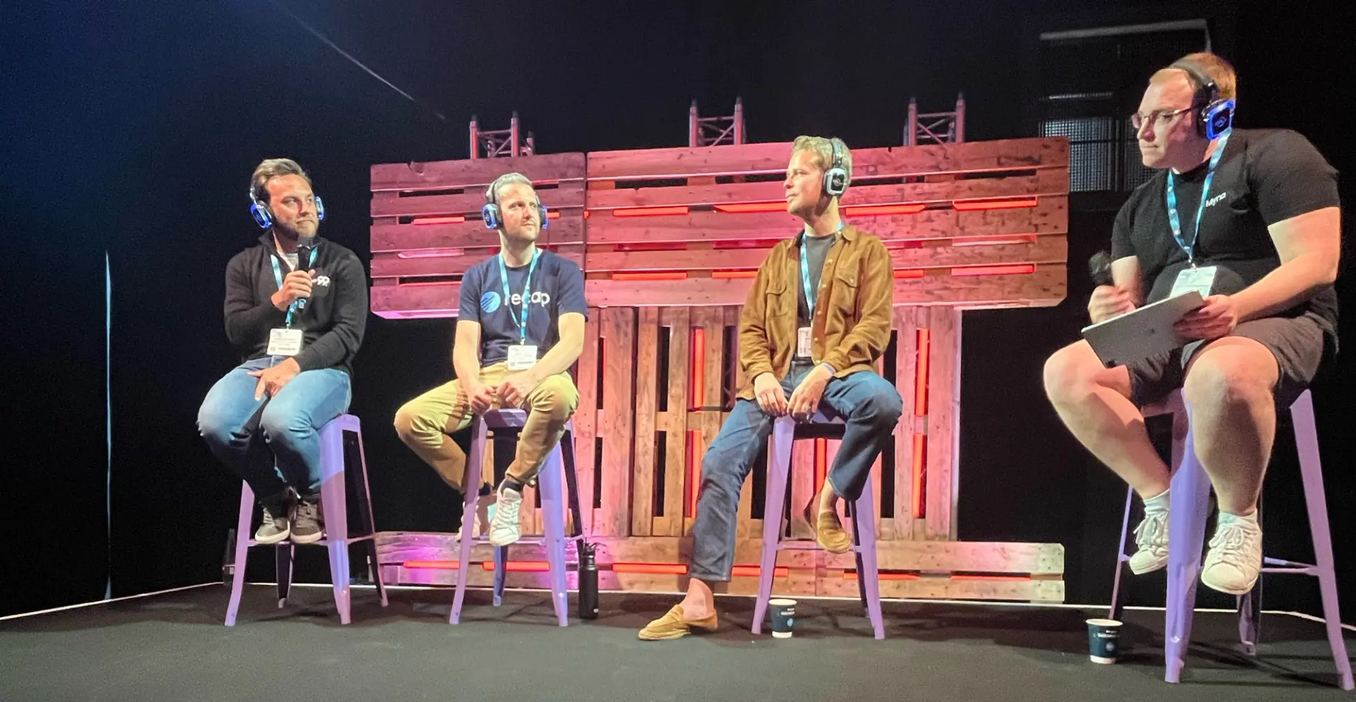 Four males from Wealth 99, Recap, Cryptio and Myna chatting on stage with headphones and microphone.