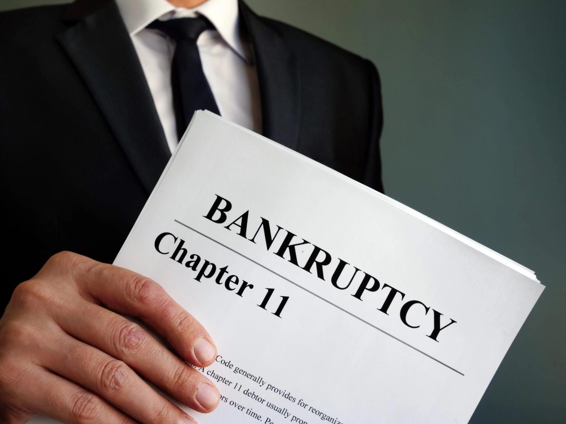 White male in suit and tie holding chapter 11 bankruptcy papers