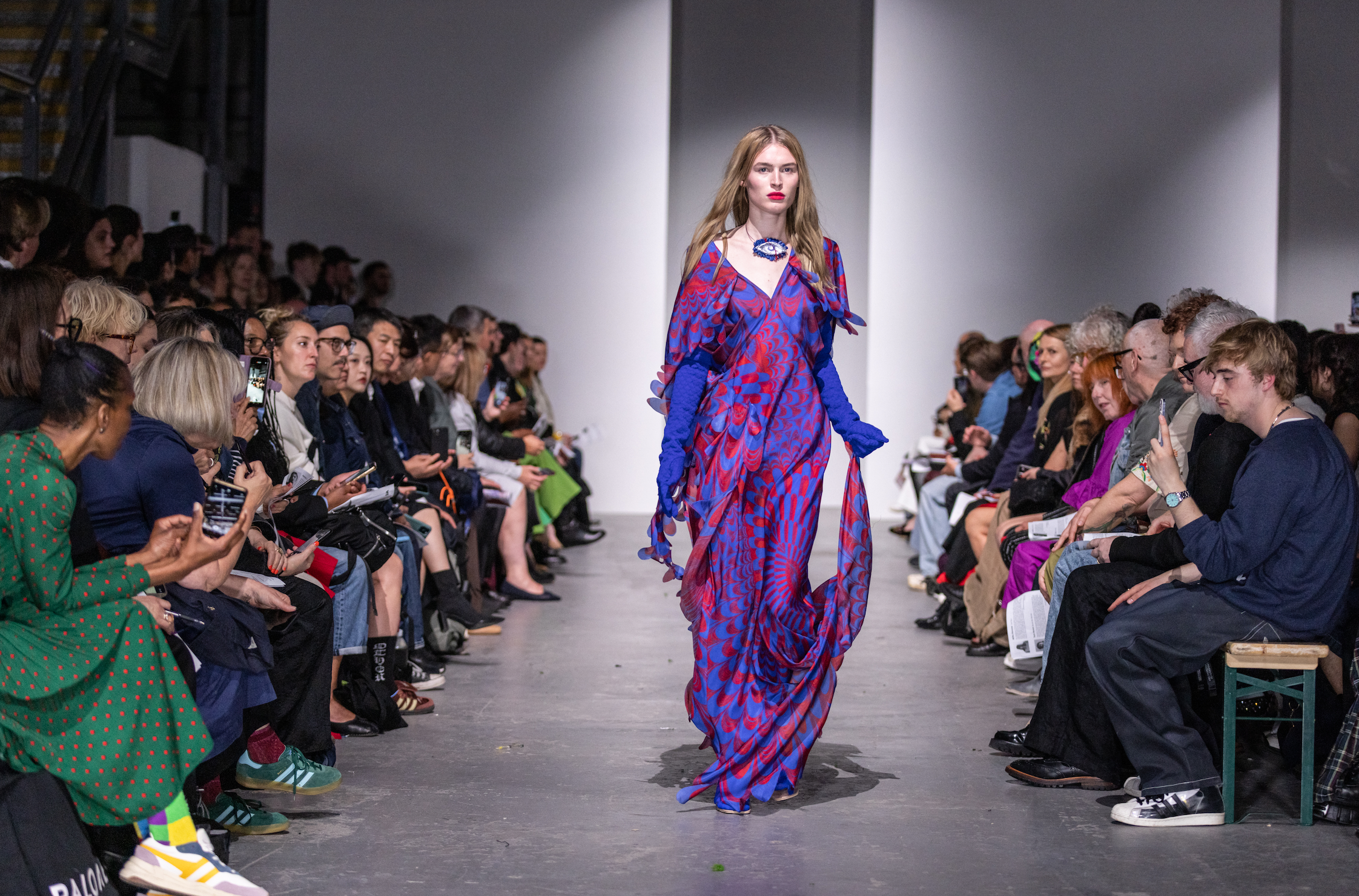 Woman in a purple and red dress walking down the catwalk at the Westminster Fashion Students' Catwalk Show.