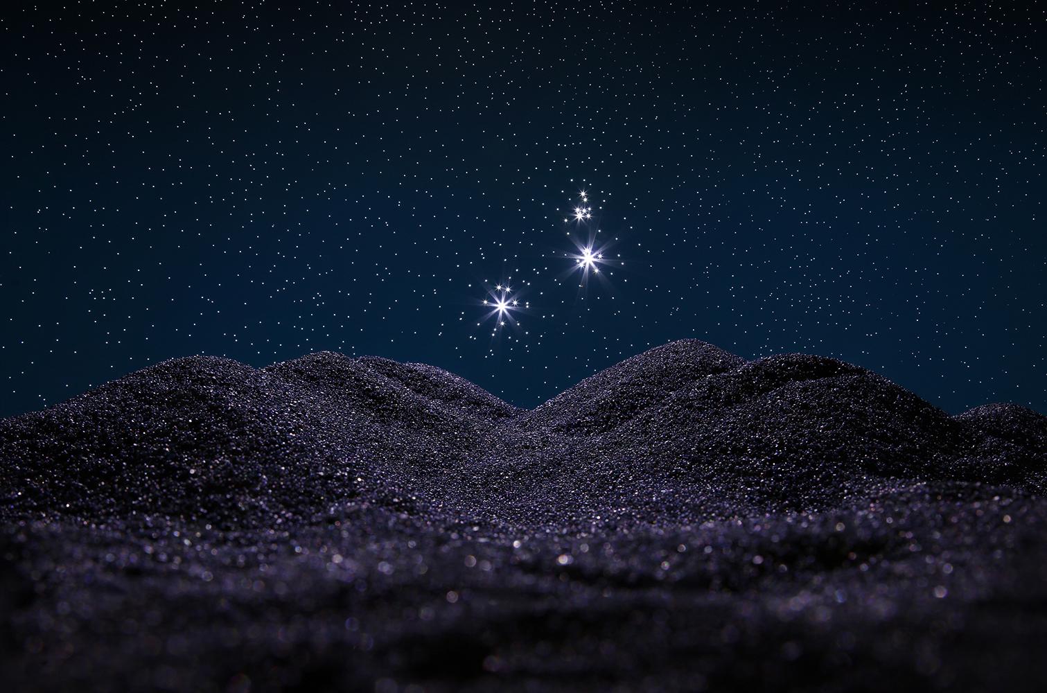 Photograph of hills taken at night. Stars are shining brightly in the nighttime sky. A photograph by Christian Jago.