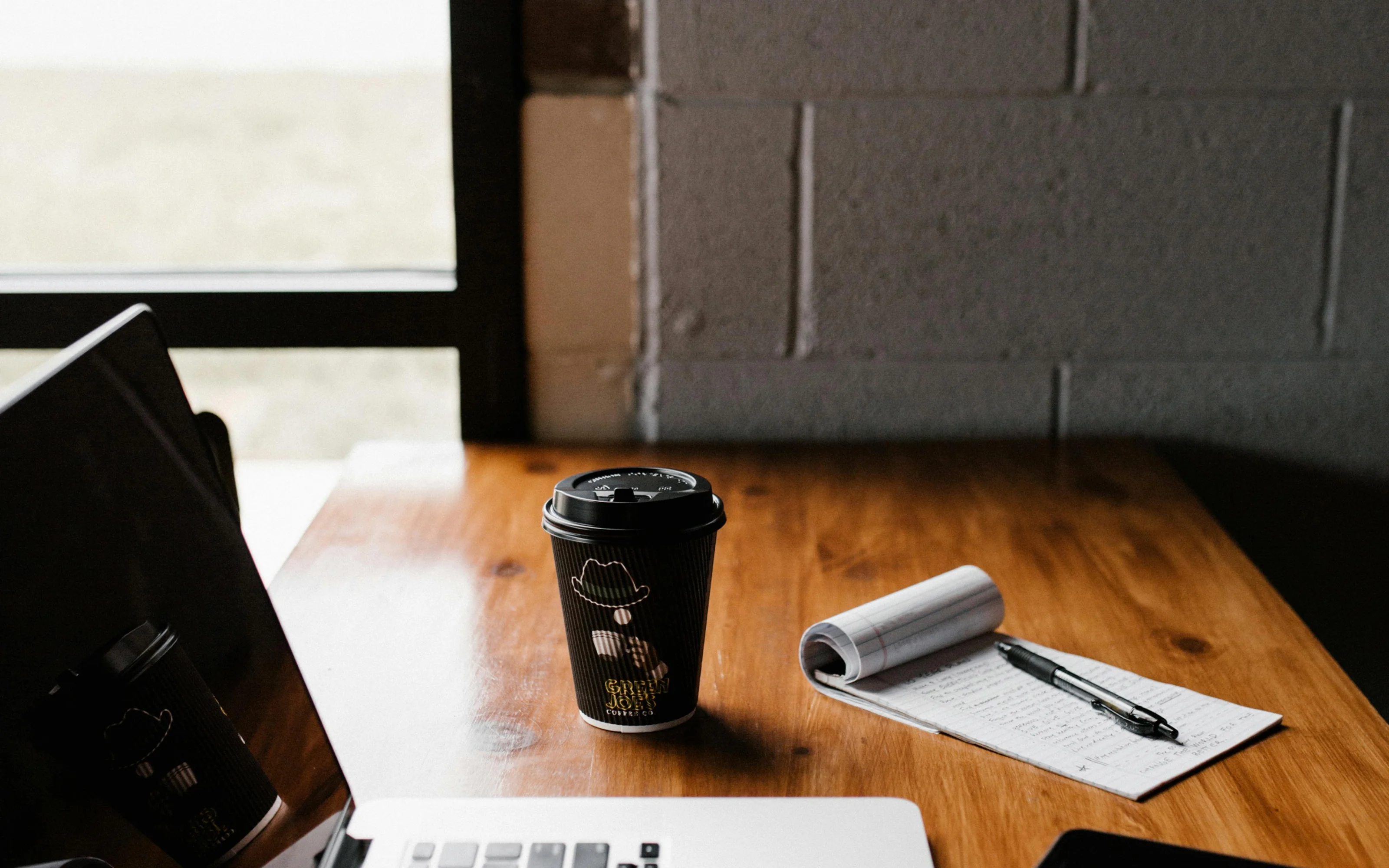 Laptop next to a coffee cup, notepad and a mobile phone