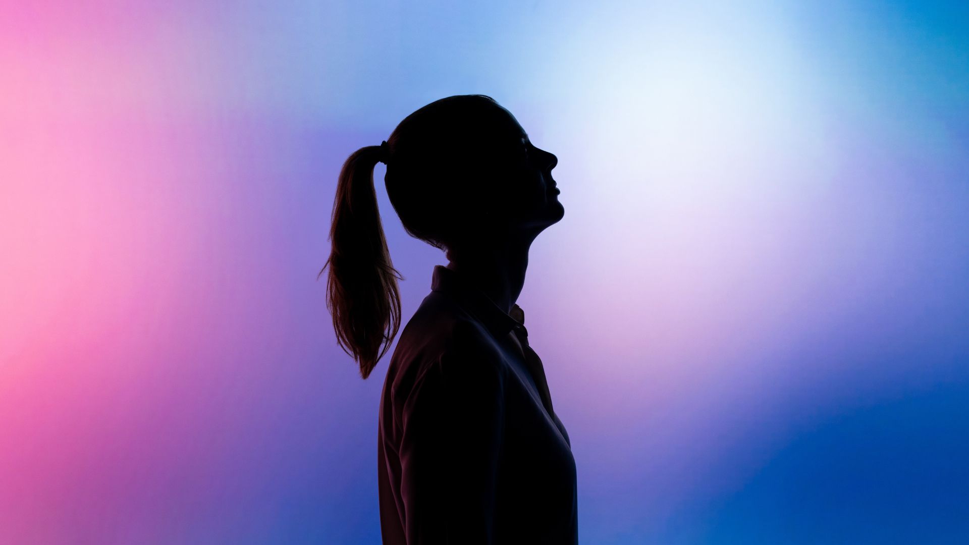 Silhouette of a woman with a ponytail against a pink and blue background.