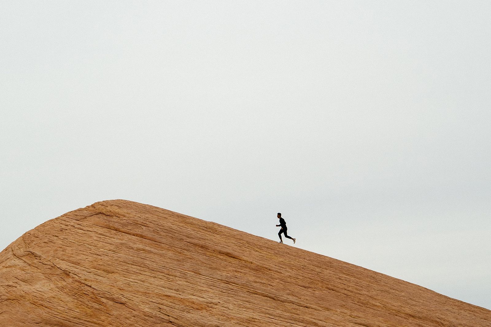 A person runs up a red rock formation against a grey sky.