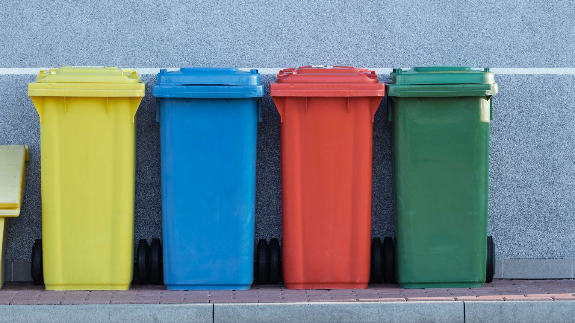Yellow, blue, red and green bins in a row along a sidewalk.