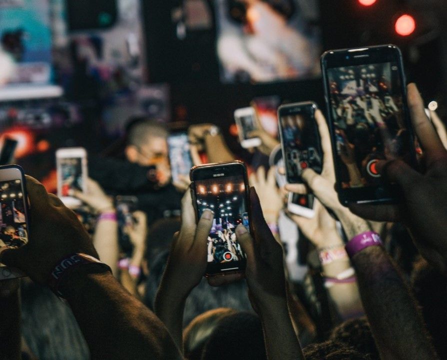 Hands in a crowd holding smartphones in the air recording a performance.