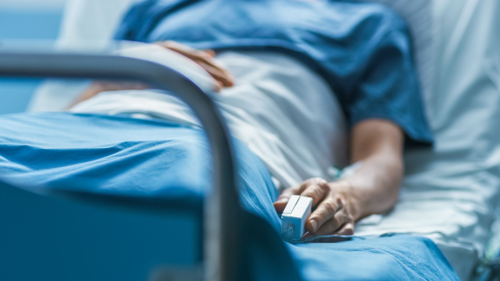 Person laying in a hospital bed with a pulse oximeter on their left index finger. 