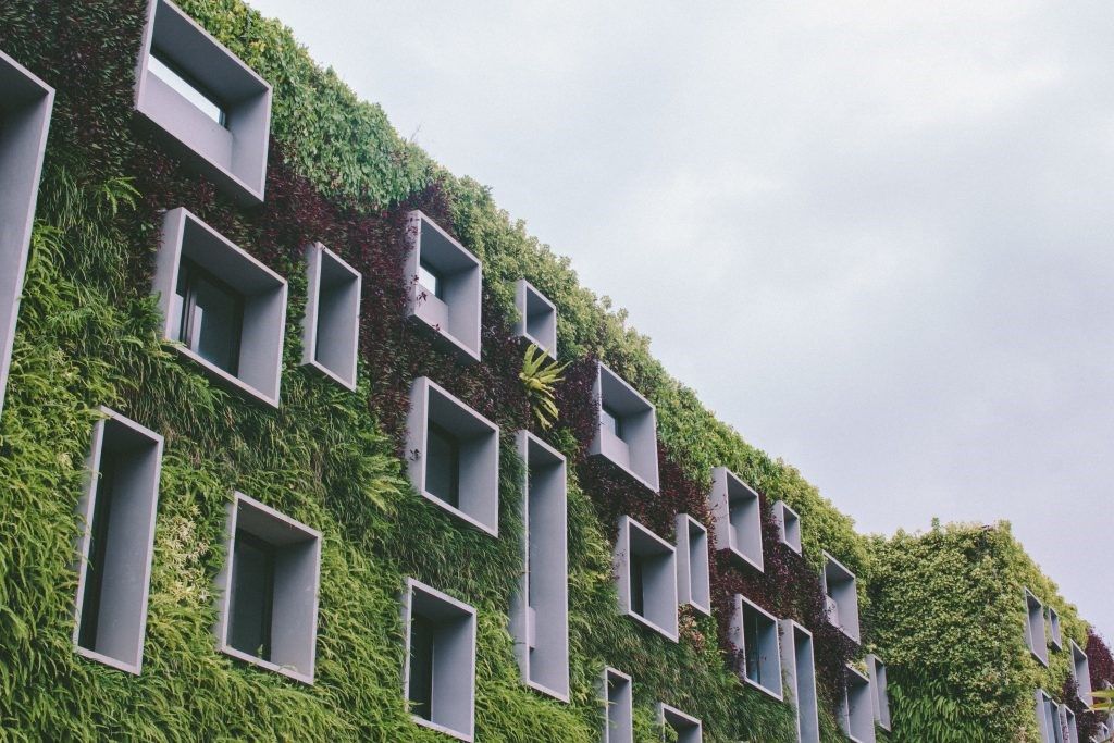 Low rise building covered in green plants against a grey sky. 