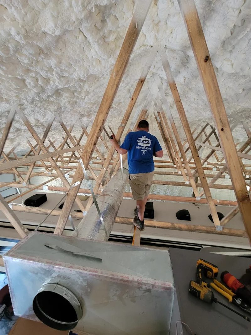 Watson Heating + Cooling technician running ductwork in an attic with spray-foam insulation