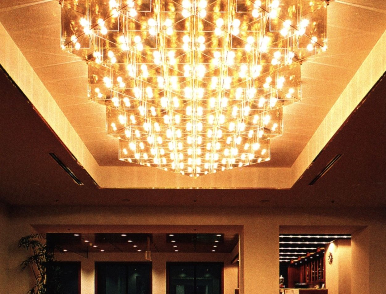 A tiered crystal chandelier blazes over a warmly lit hotel lobby.
