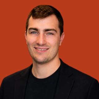Jeff Long, smiling, in a black blazer and black T-shirt against a rust background.