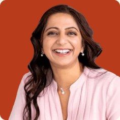 Kady Srinivasan, smiling, in a pale pink blouse against a rust background.
