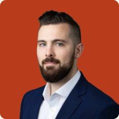 Garrett Tubbs, bearded, in a navy blazer and white shirt against a rust background.