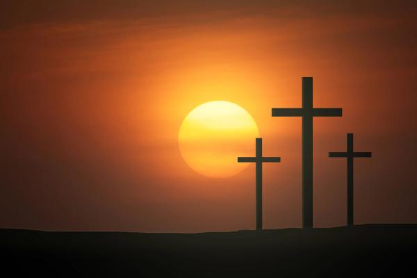 3 crosses on a hill with a sun setting behind them