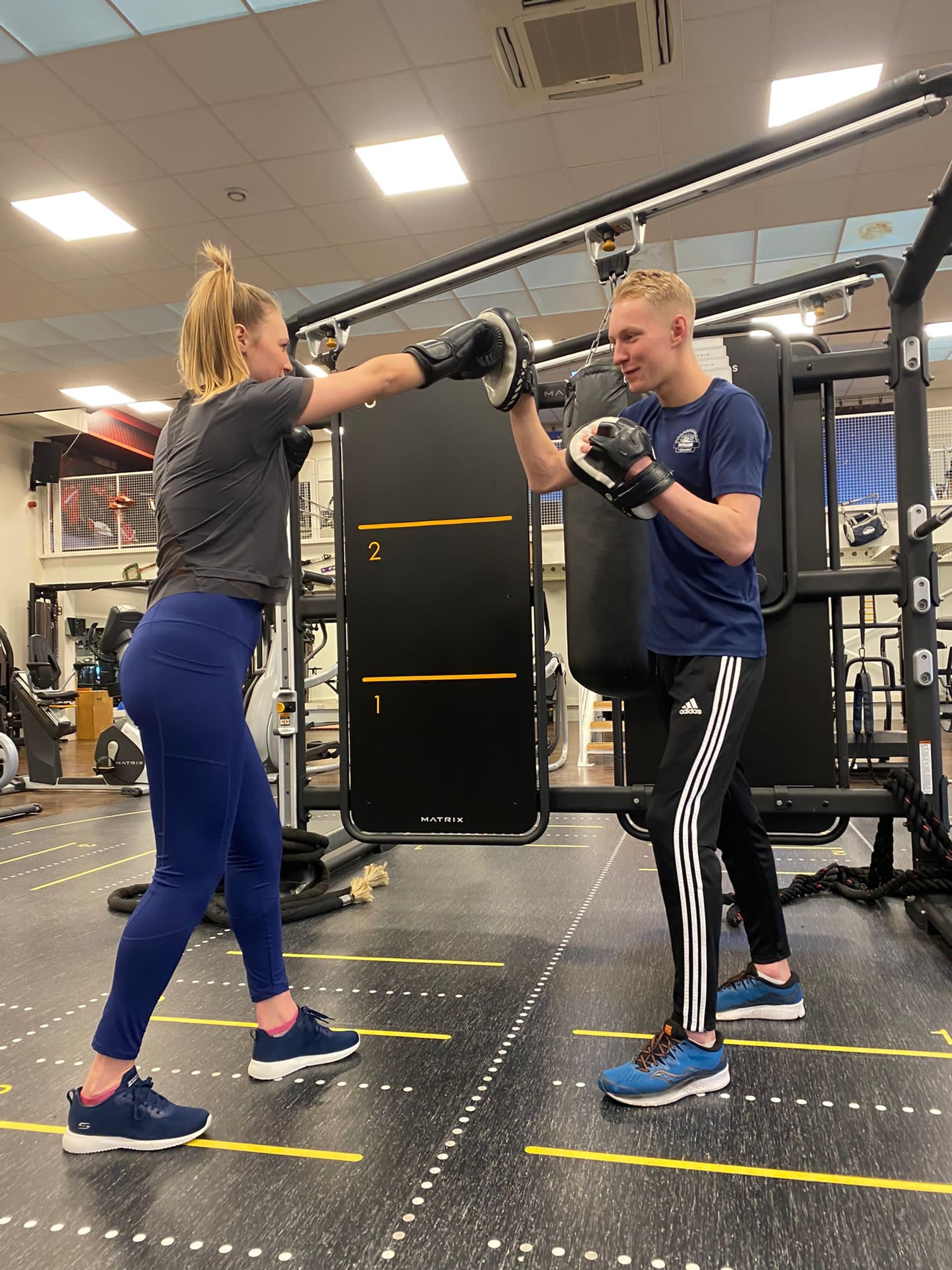 Een trainer begeleidt een vrouw tijdens een bokstraining met handschoenen in een sportschool.